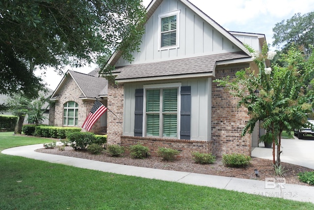 view of front facade with roof with shingles, brick siding, board and batten siding, and a front yard