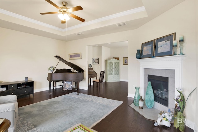 living room with a tiled fireplace, a tray ceiling, dark wood-type flooring, and ornamental molding