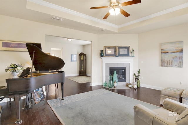 living room featuring a tile fireplace, ceiling fan, dark hardwood / wood-style floors, a tray ceiling, and ornamental molding