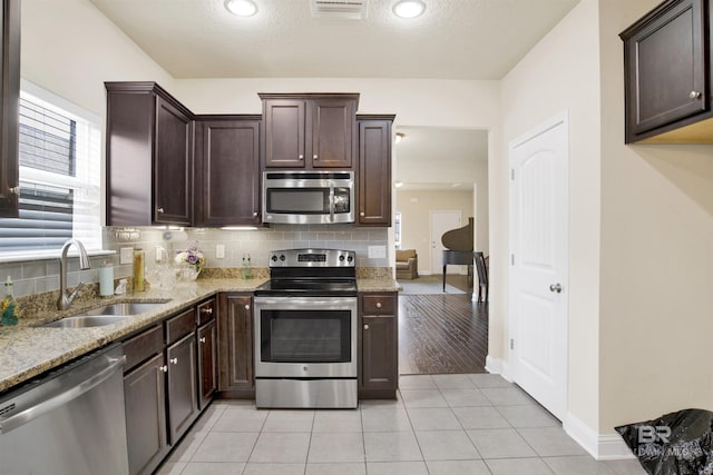 kitchen with sink, light tile patterned floors, appliances with stainless steel finishes, light stone countertops, and decorative backsplash