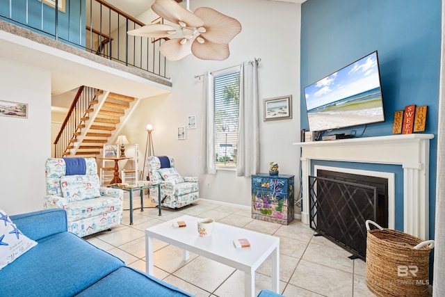 living room with ceiling fan, a fireplace, a towering ceiling, stairway, and tile patterned floors