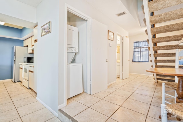 kitchen with light tile patterned floors, white electric range oven, visible vents, and stacked washer and clothes dryer