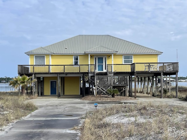 coastal inspired home with metal roof, a carport, a wooden deck, and driveway