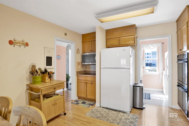 kitchen with freestanding refrigerator, light wood-style floors, dobule oven black, stainless steel microwave, and tasteful backsplash