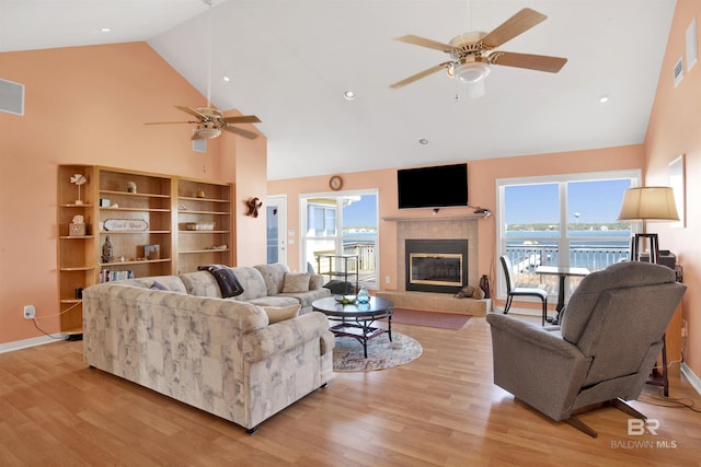 living area with baseboards, a fireplace, light wood-type flooring, and high vaulted ceiling