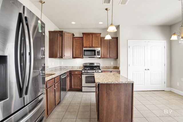 kitchen featuring pendant lighting, appliances with stainless steel finishes, light tile patterned flooring, and a center island