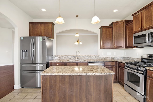 kitchen with a kitchen island, light tile patterned flooring, arched walkways, stainless steel appliances, and a sink