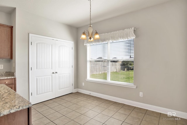 unfurnished dining area featuring an inviting chandelier, light tile patterned floors, and baseboards