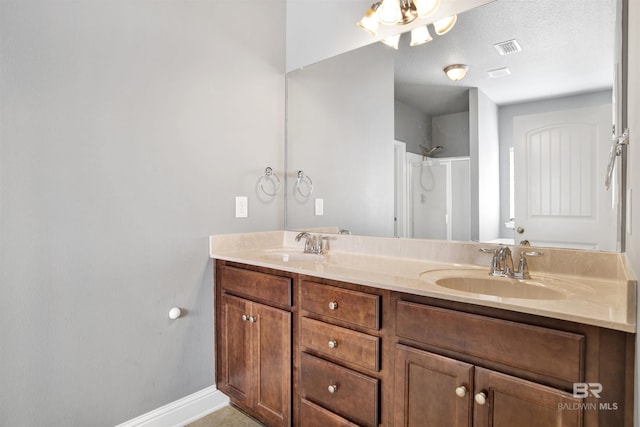 bathroom with double vanity, visible vents, walk in shower, and a sink