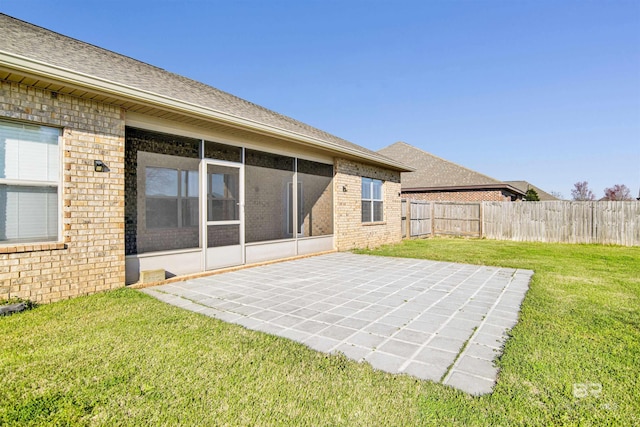 rear view of house featuring brick siding, fence, a lawn, a sunroom, and a patio