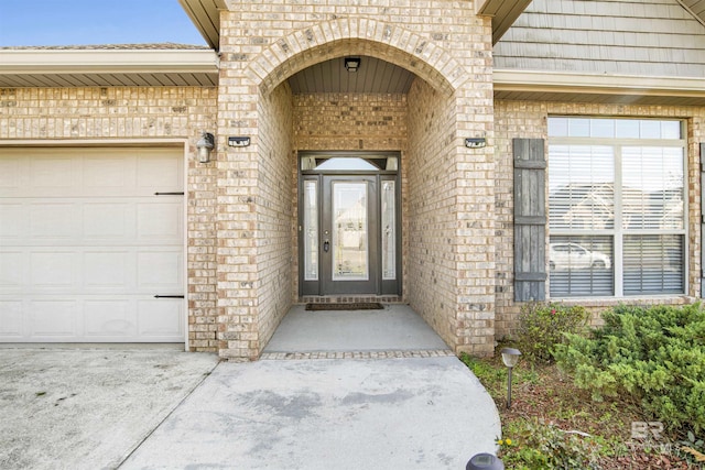 entrance to property with brick siding, an attached garage, and concrete driveway