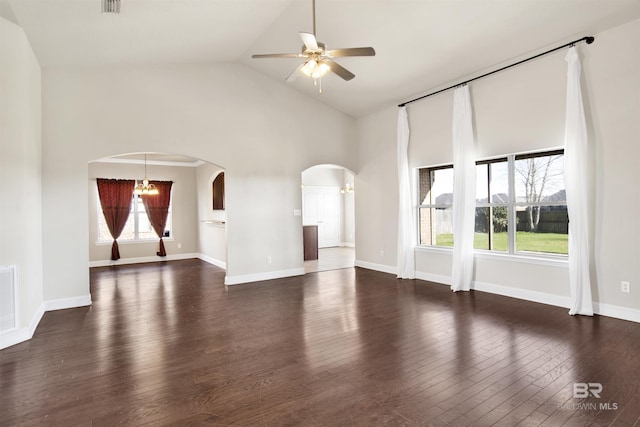 unfurnished living room with arched walkways, ceiling fan with notable chandelier, baseboards, and dark wood-style flooring