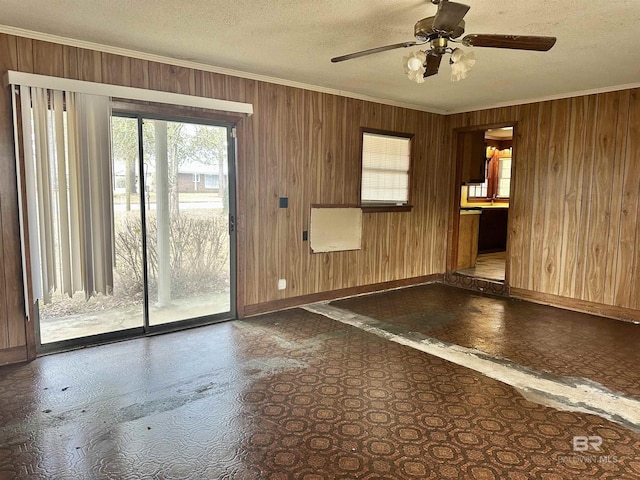 unfurnished room featuring wood walls, a textured ceiling, baseboards, and crown molding