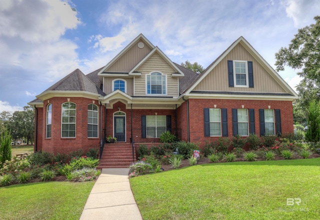 view of front facade featuring a shingled roof, a front yard, a porch, and brick siding