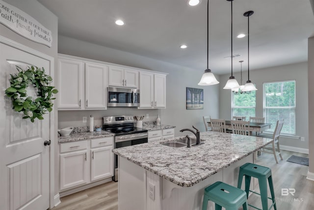 kitchen featuring light stone countertops, white cabinetry, a sink, light wood-style flooring, and stainless steel appliances