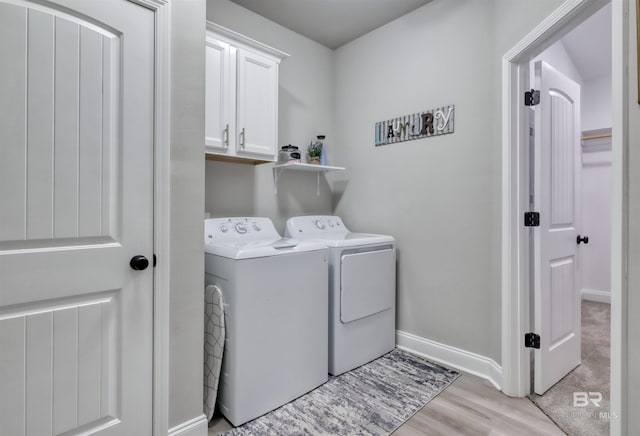 clothes washing area featuring light wood-type flooring, cabinet space, baseboards, and washing machine and clothes dryer