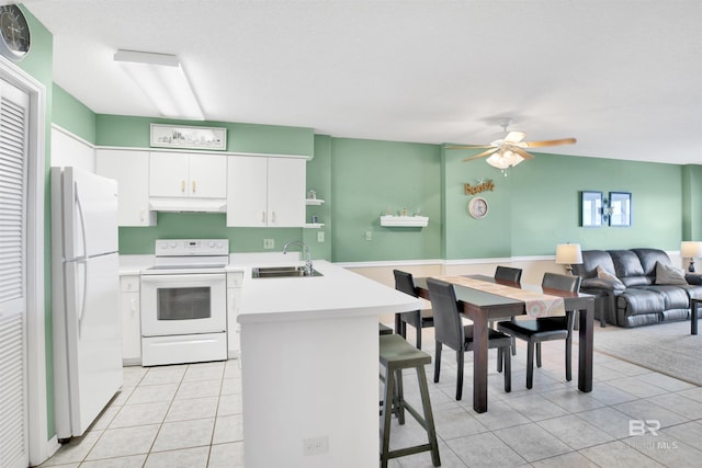 kitchen with a breakfast bar, a sink, a peninsula, white appliances, and under cabinet range hood