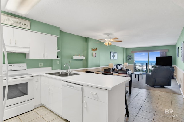 kitchen with white appliances, open floor plan, a peninsula, under cabinet range hood, and a sink