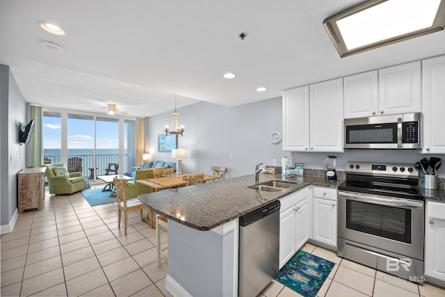 kitchen with appliances with stainless steel finishes, open floor plan, white cabinets, a sink, and a peninsula