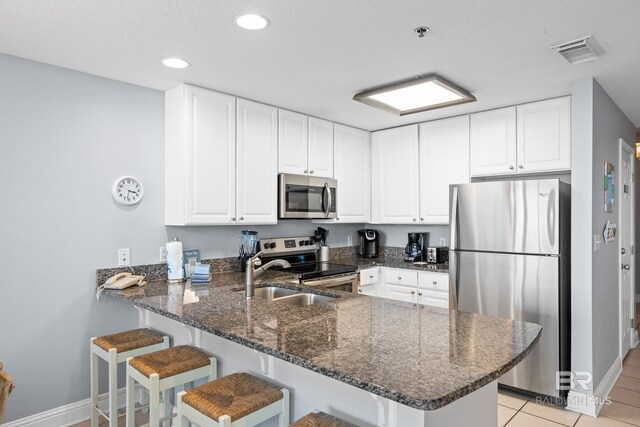 kitchen with stainless steel appliances, a peninsula, a sink, visible vents, and dark stone countertops