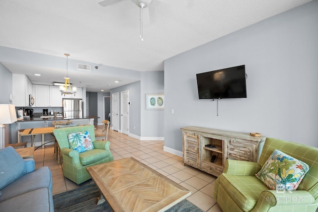 living room with light tile patterned floors, a textured ceiling, ceiling fan with notable chandelier, visible vents, and baseboards