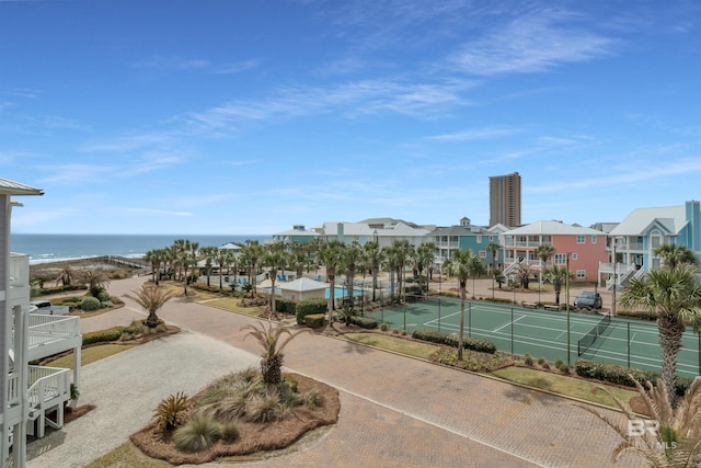 exterior space with a tennis court, fence, and a water view