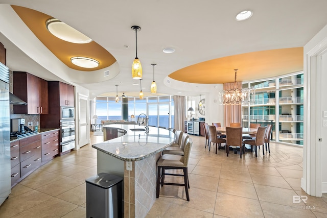 kitchen with pendant lighting, light tile patterned flooring, sink, a spacious island, and light stone countertops