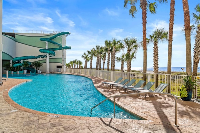 view of swimming pool with a water slide, a water view, and a patio area