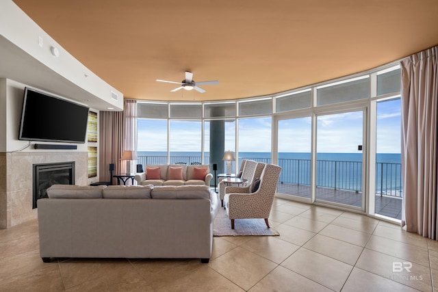 tiled living room with a water view, ceiling fan, a wall of windows, and a fireplace