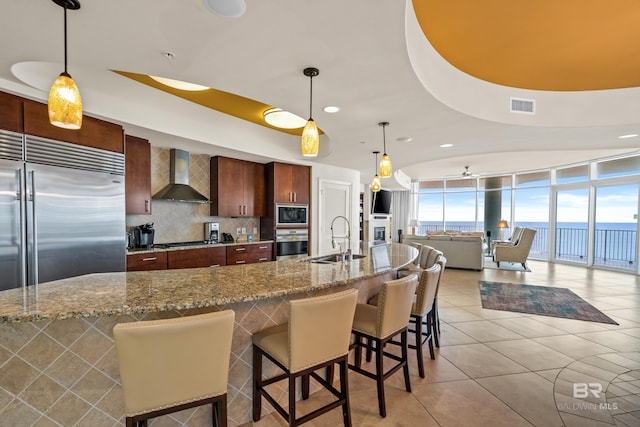 kitchen with wall chimney exhaust hood, a healthy amount of sunlight, built in appliances, and sink