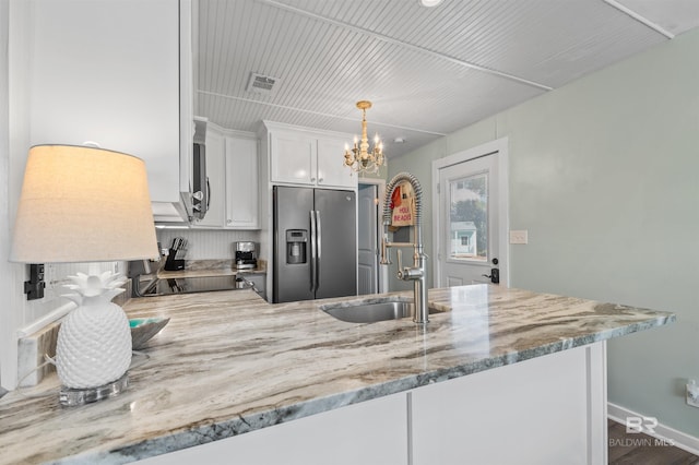 kitchen with light stone counters, a peninsula, stainless steel refrigerator with ice dispenser, white cabinets, and a sink