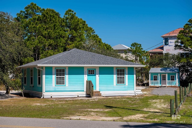 view of front of home with a front yard, an outdoor structure, and roof with shingles