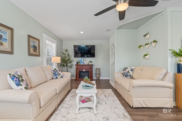 living area featuring baseboards, visible vents, dark wood finished floors, ceiling fan, and a glass covered fireplace