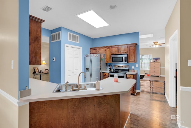 kitchen with ceiling fan, sink, kitchen peninsula, wood-type flooring, and stainless steel appliances