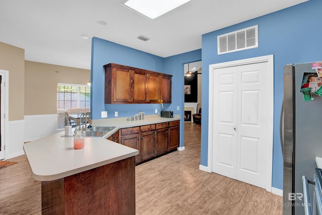 kitchen with stainless steel fridge, kitchen peninsula, sink, and light hardwood / wood-style flooring