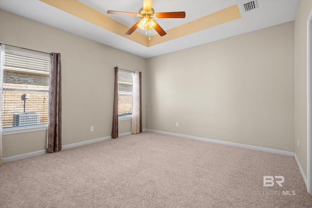 carpeted spare room with a tray ceiling, ceiling fan, and plenty of natural light