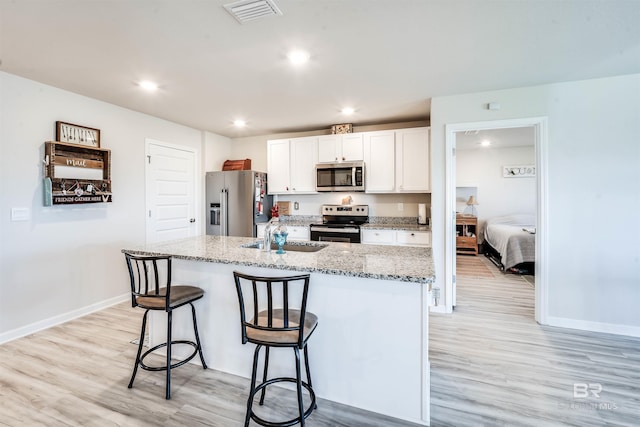 kitchen with a breakfast bar, a sink, white cabinets, appliances with stainless steel finishes, and a center island with sink