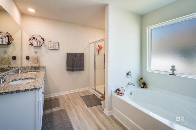 full bath featuring a bath, double vanity, a sink, and wood finished floors