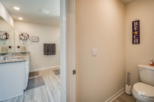 bathroom with toilet, recessed lighting, wood finished floors, vanity, and baseboards