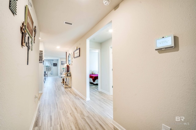 hall with visible vents, light wood-style flooring, and baseboards