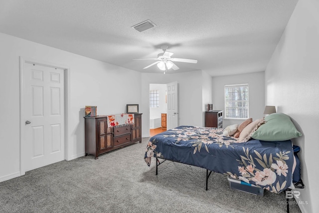 carpeted bedroom featuring a textured ceiling, ensuite bathroom, a ceiling fan, visible vents, and baseboards