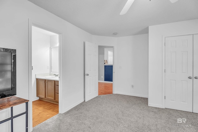 unfurnished bedroom featuring a textured ceiling, connected bathroom, light colored carpet, a sink, and baseboards