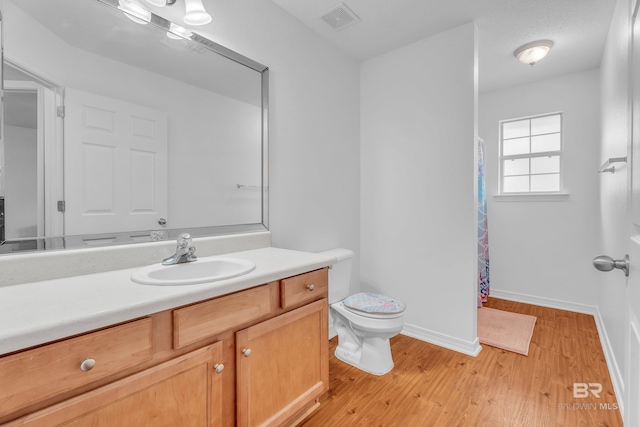 bathroom featuring baseboards, visible vents, toilet, wood finished floors, and vanity