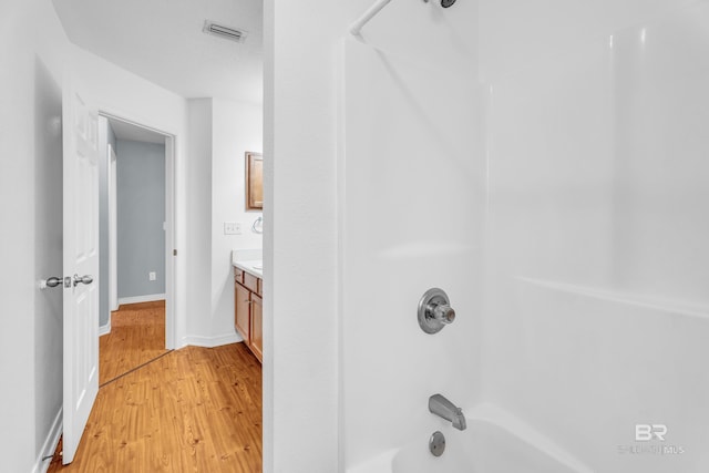 full bathroom featuring visible vents, vanity, wood finished floors,  shower combination, and baseboards