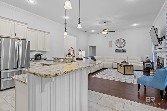 kitchen with crown molding, stainless steel fridge, light wood-type flooring, decorative light fixtures, and white cabinetry