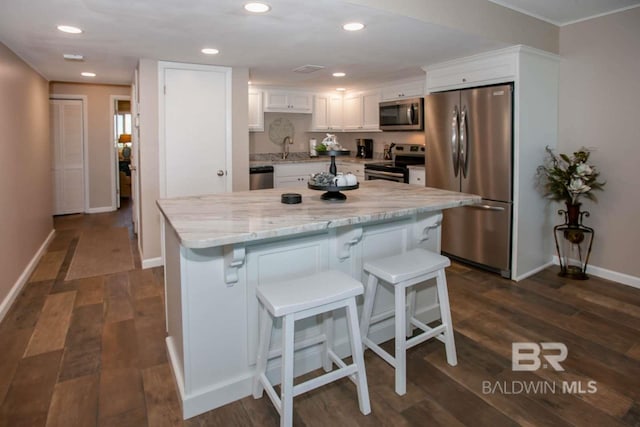 kitchen with appliances with stainless steel finishes, a kitchen bar, white cabinetry, light stone countertops, and dark hardwood / wood-style floors