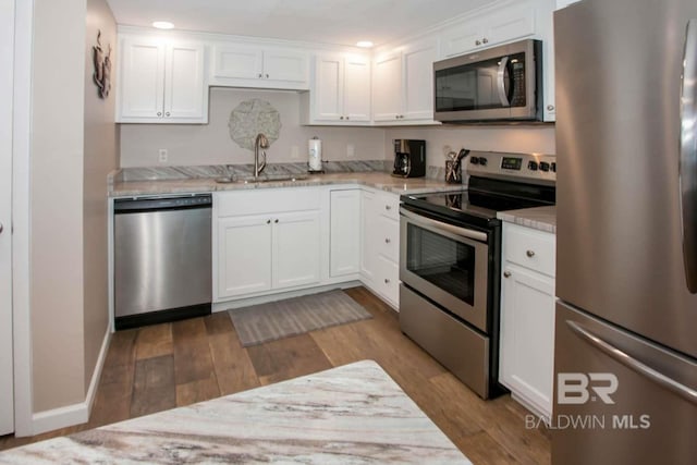 kitchen featuring light wood-type flooring, light stone counters, stainless steel appliances, sink, and white cabinetry