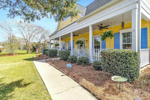 entrance to property with a porch, a yard, roof with shingles, and ceiling fan