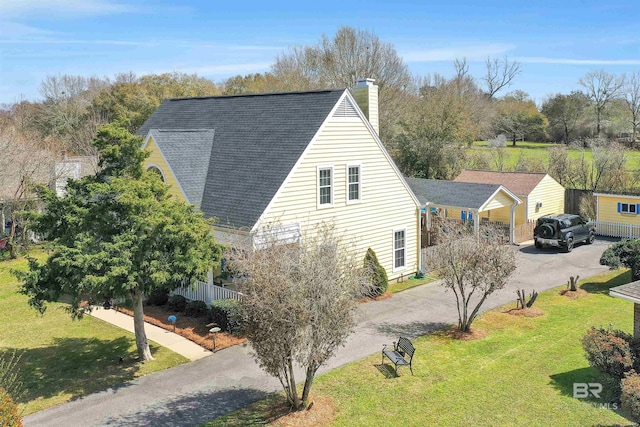 view of property exterior with driveway, a lawn, roof with shingles, and a chimney