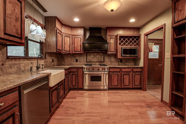 kitchen with sink, stainless steel appliances, light hardwood / wood-style flooring, decorative light fixtures, and custom range hood